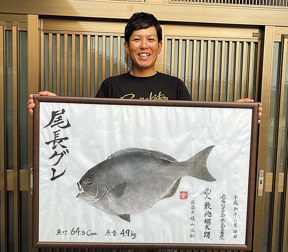 自己記録・
64.5cmの尾長グレの魚拓を手に笑顔の敷地