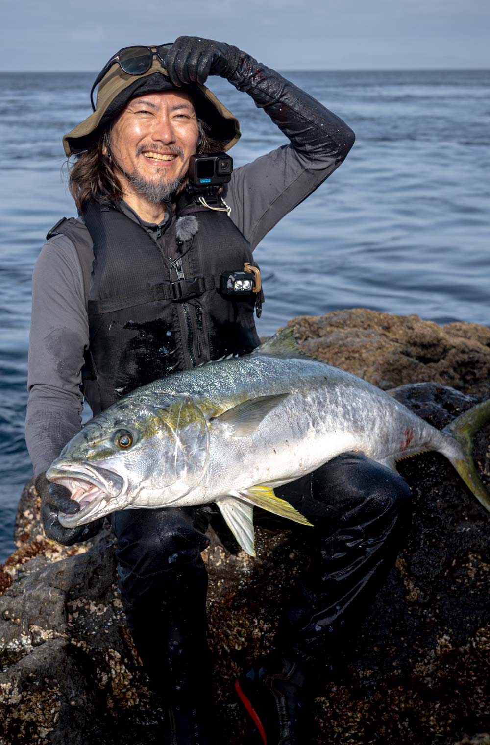 釣り上げたヒラマサを膝に乗せ、満面の笑みを見せる松本