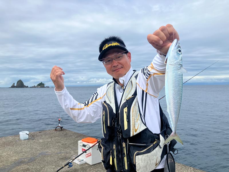 ラインを持ち、釣り上げた魚を掲げる鷲尾