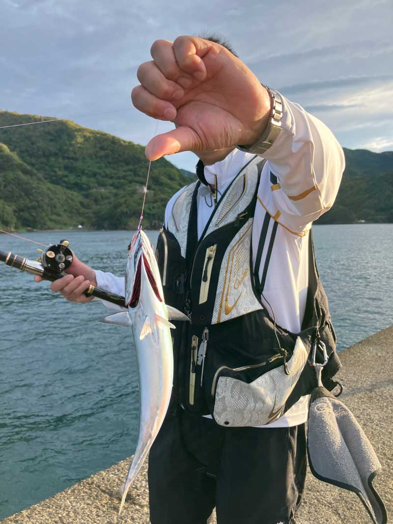 ラインを持ち、釣り上げた魚を掲げる鷲尾