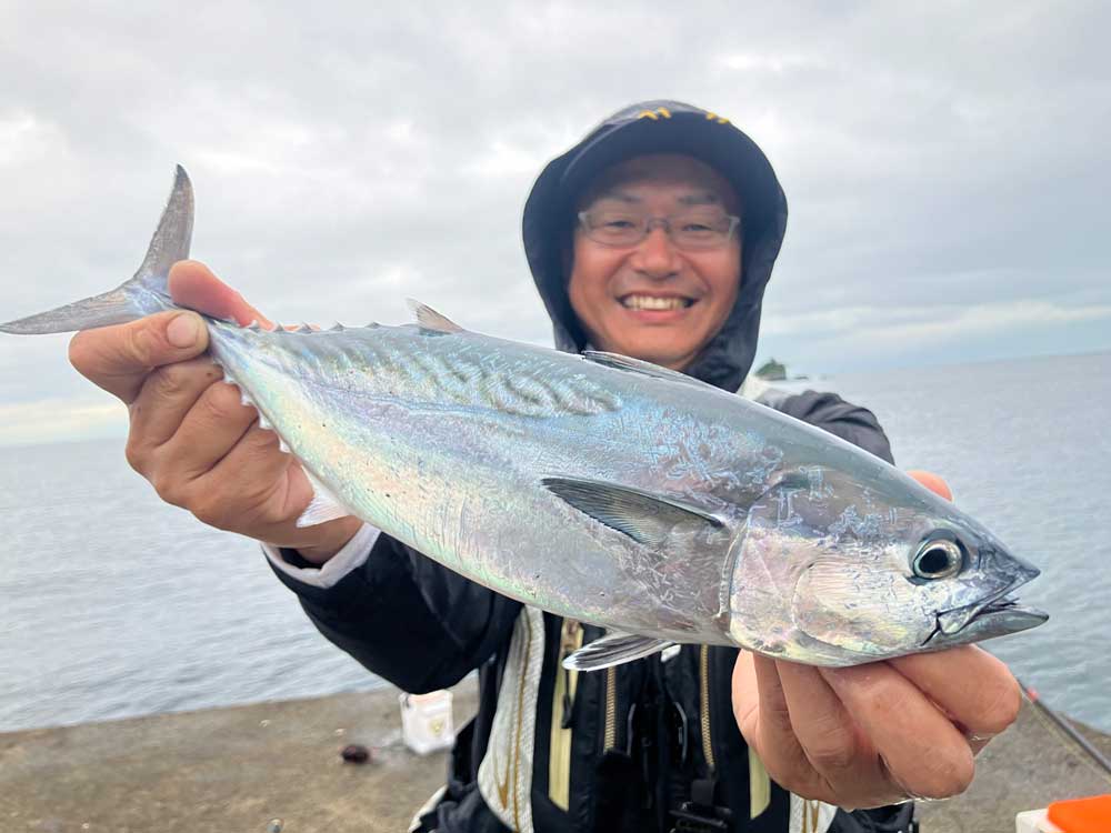 スマガツオと思われる魚を両手に、笑顔を浮かべる鷲尾