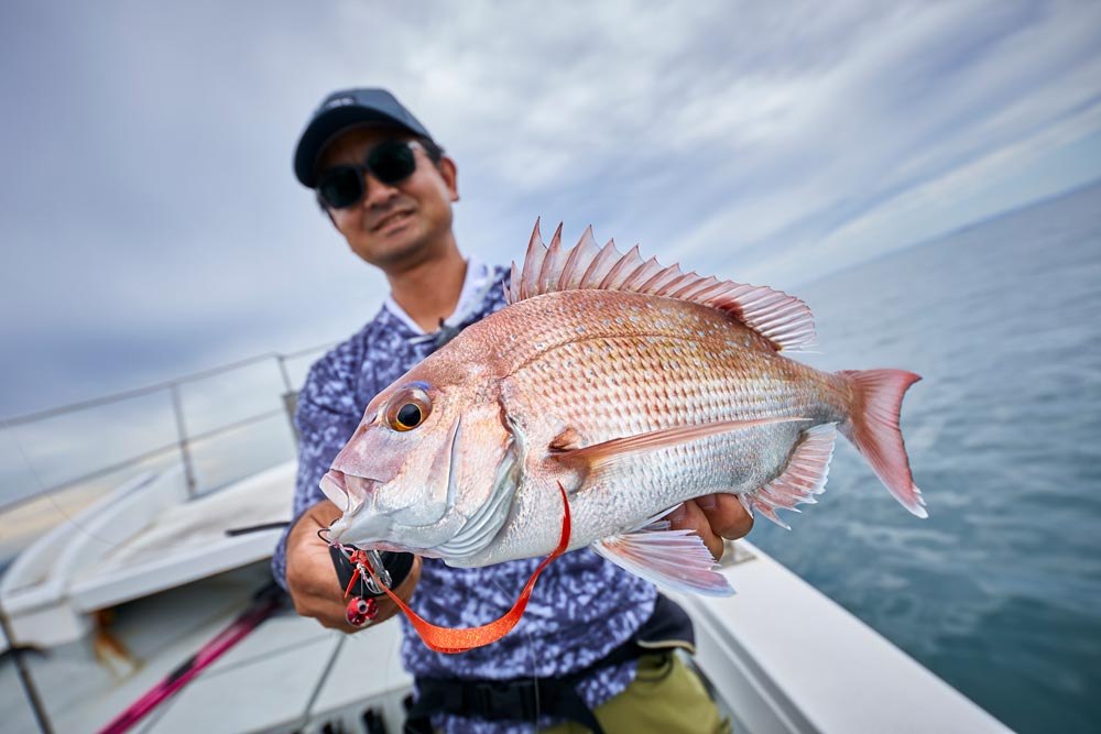 釣り上げたタイを両手で掲げ笑顔を見せる男性