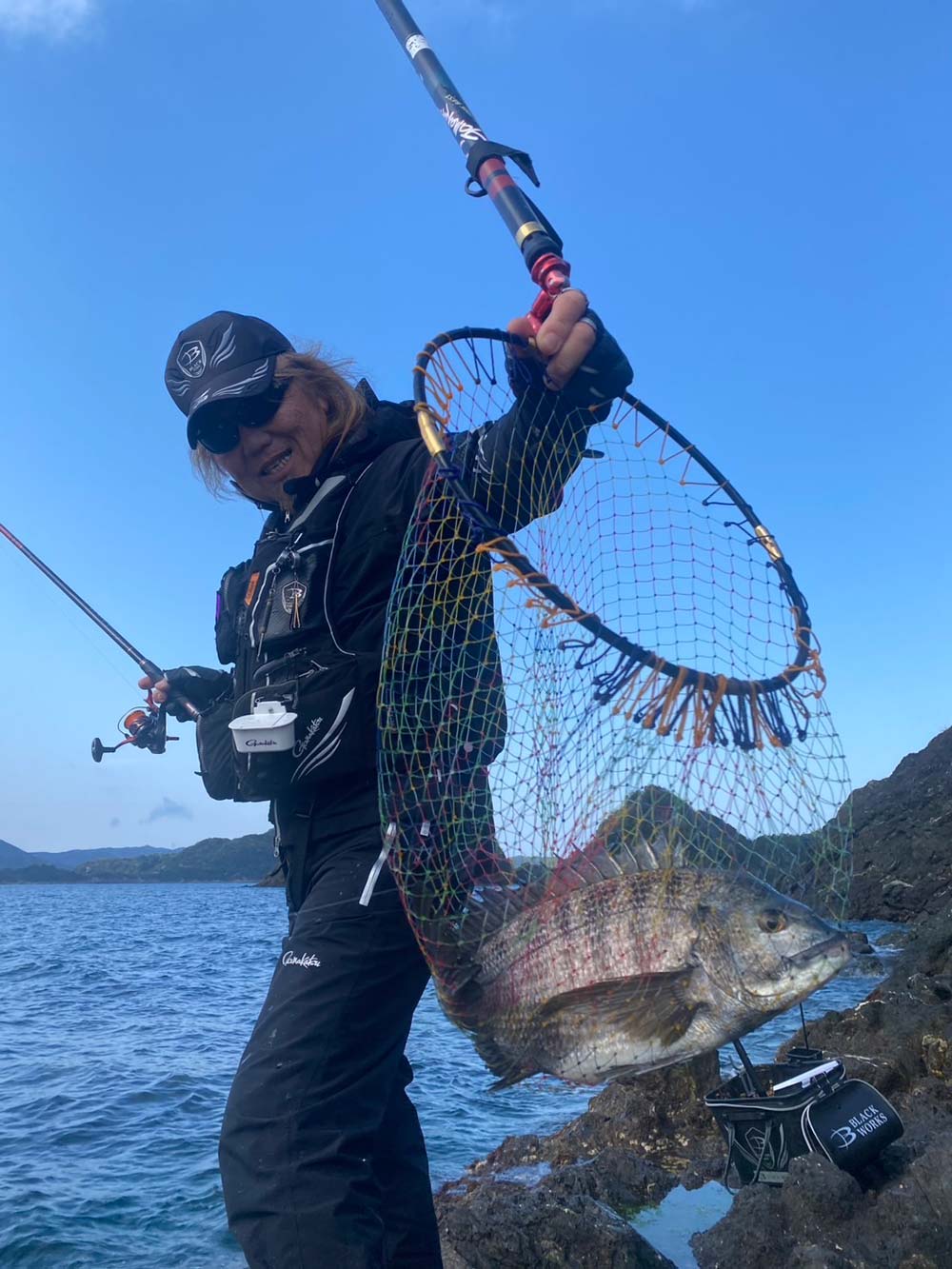 釣り上げたチヌが収まったタモ網を掲げ、笑顔を見せる前西