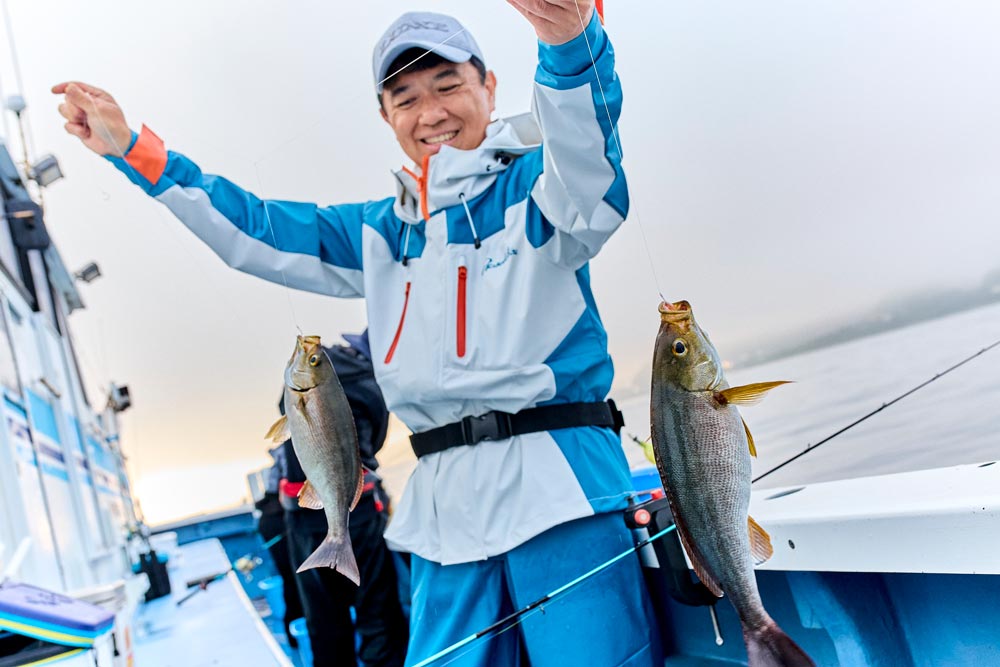 船上、魚を釣り上げて笑顔を見せる、レインスーツを着た男性