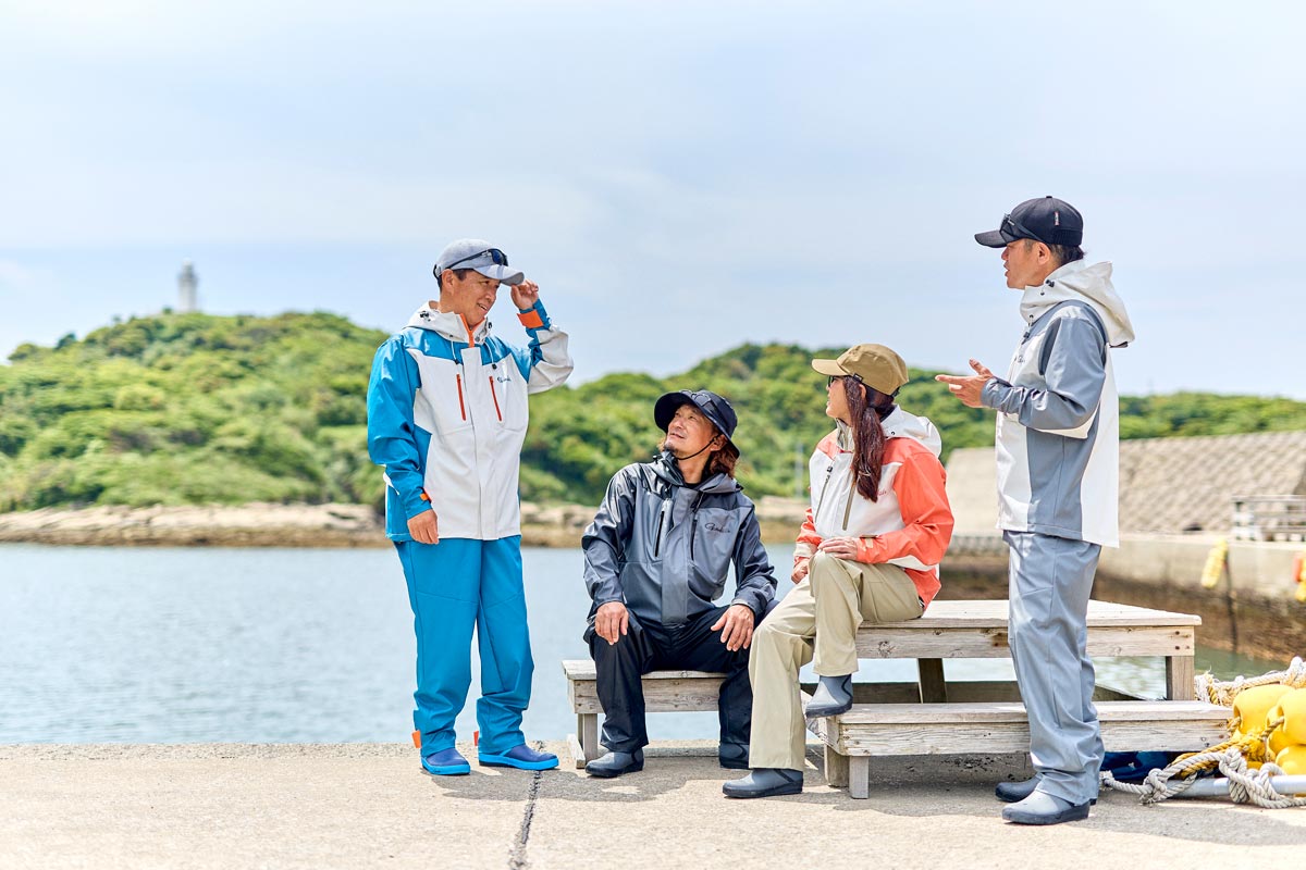 レインスーツを着用した男女4名のモデルが、堤防で談笑する様子