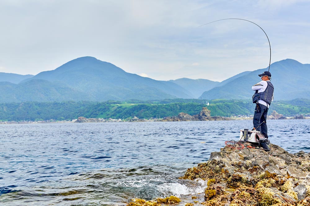 大きな弧を描く竿を操作する久保野