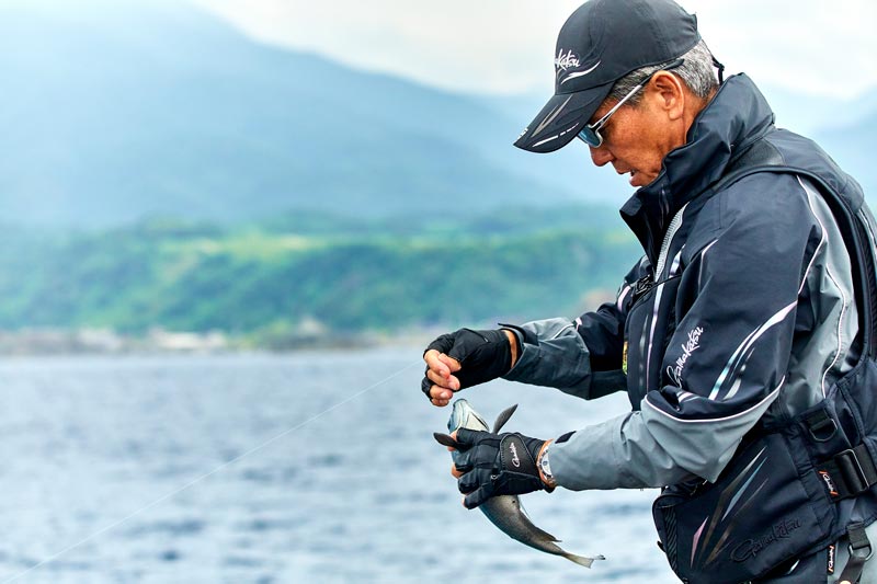 釣り上げた口太の唇から鈎を外そうとしている久保野