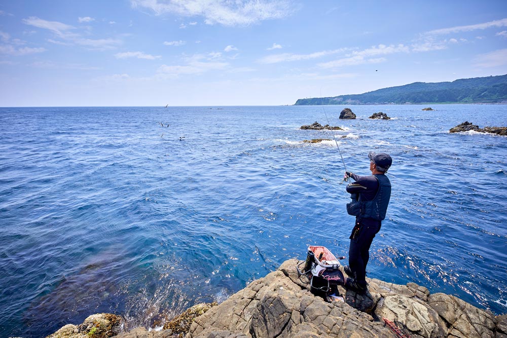 磯先に立ち、竿を振る久保野。奥の海面では魚が跳ねているのがわかる。