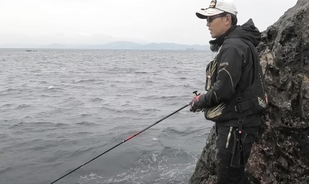 岩礁壁に立ち、海の様子を窺いながら竿を操作する敷地