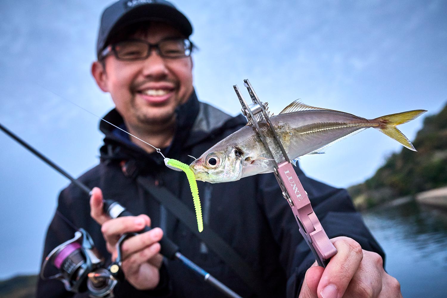 右手に竿、左手に釣り上げたアジを手に笑顔を見せる藤原