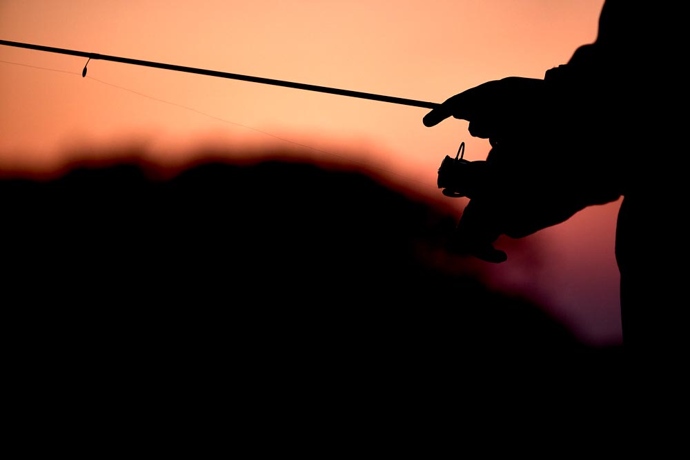 夕暮れ時の釣り。竿とそれを操作する手元の影