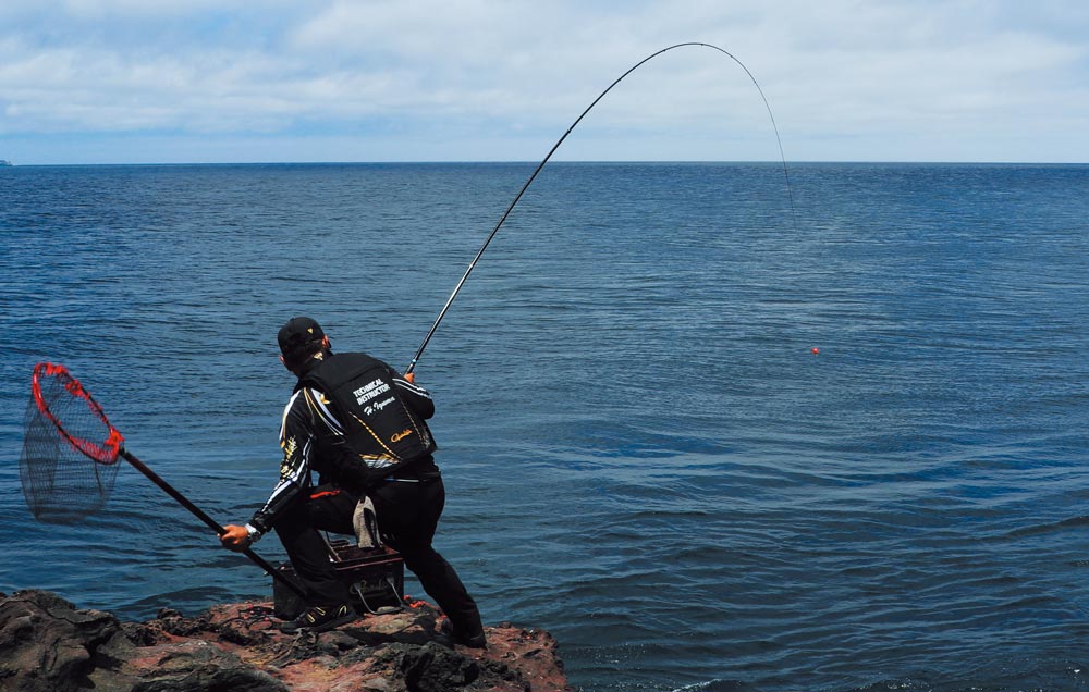 右手で大きく湾曲する竿を操り魚とやりとりしながら、左手でタモ網を拾った猪熊の背中