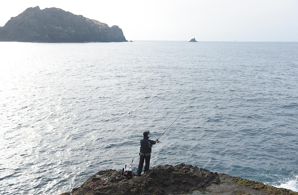 海原の広がる磯に立ち、グレスペシャルFでテスト釣りを行う久保野