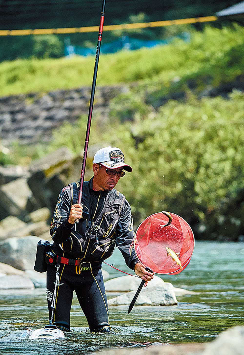 釣り上げた川魚2匹をタモ網に入れようとしている廣岡