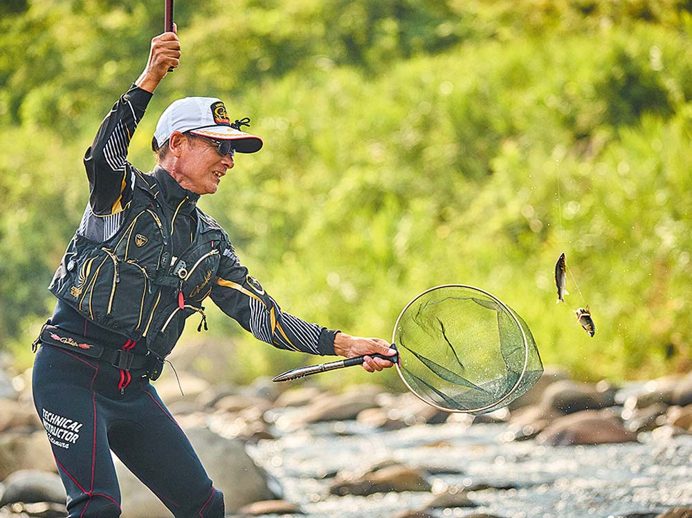 釣り上げた鮎を、タモ網に入れようとしている笑顔の北村