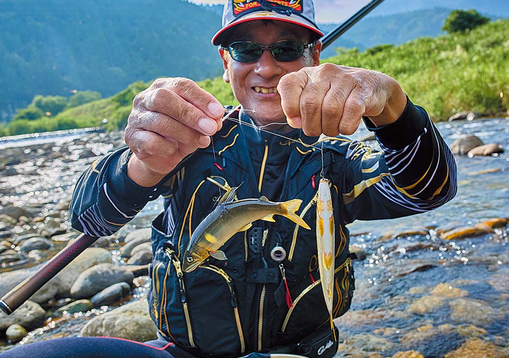 ラインを持ち、釣り上げたばかりの鮎を掲げて見せる笑顔の北村
