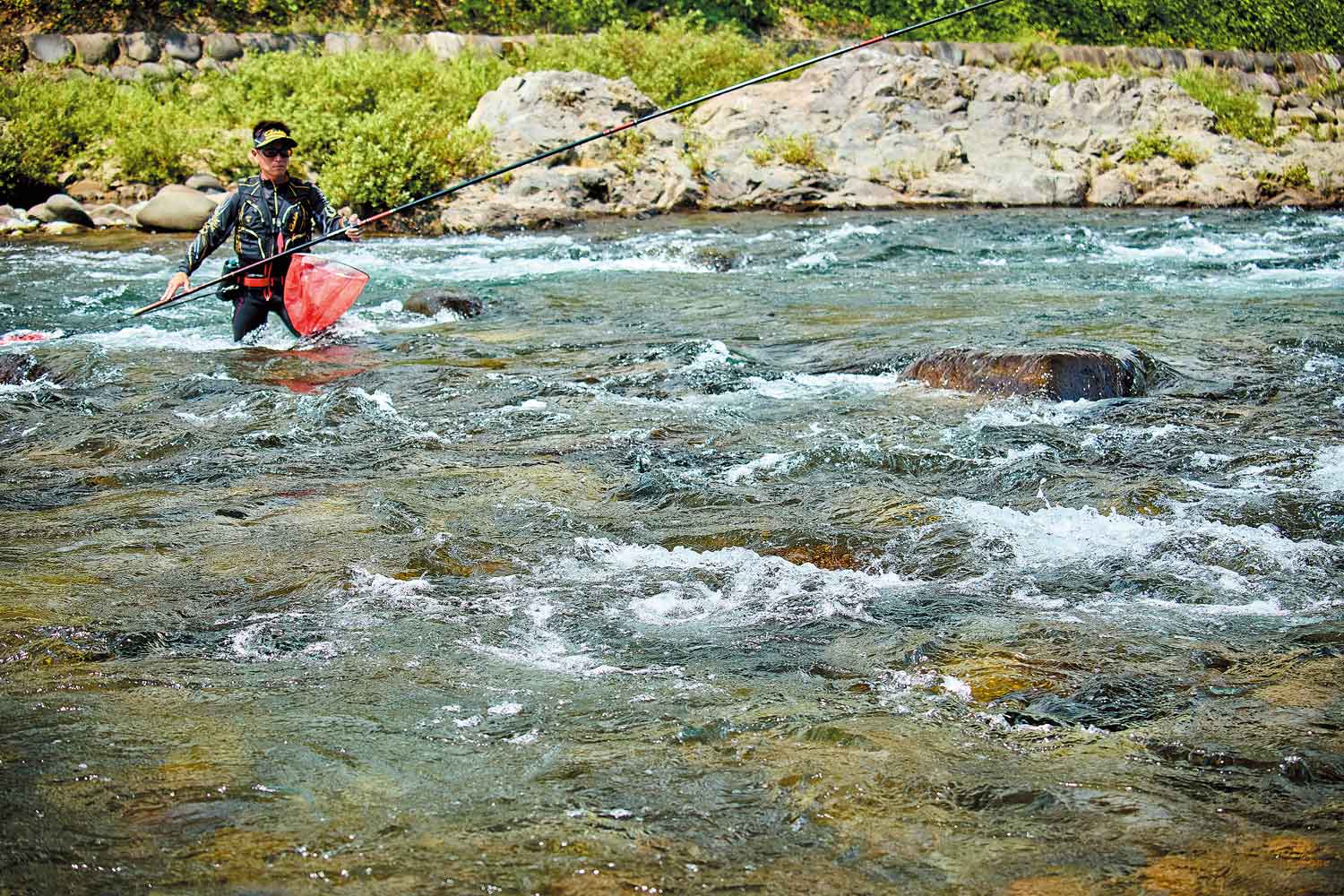 流れのある川の中へ入り、竿を構える谷口