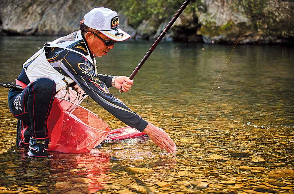 浅瀬でしゃがみ、釣り上げた魚を右手で掴もうとしている廣岡