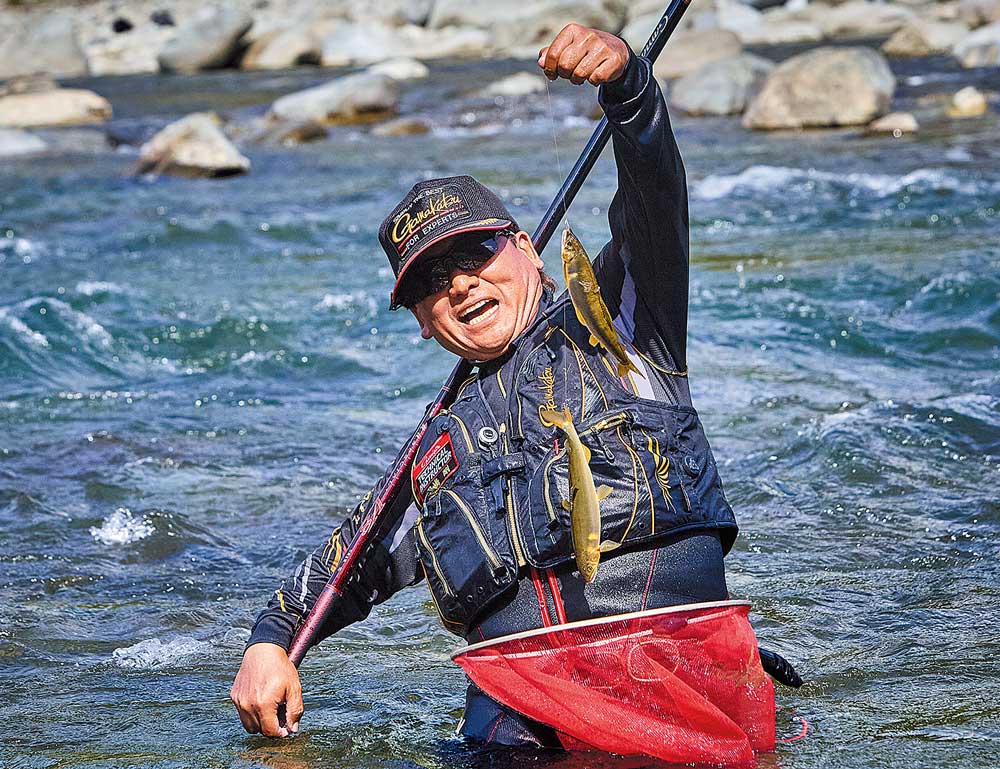 腰辺りまで浸かる深い川の中。鮎を2尾釣り上げ、満面の笑顔を見せる田嶋