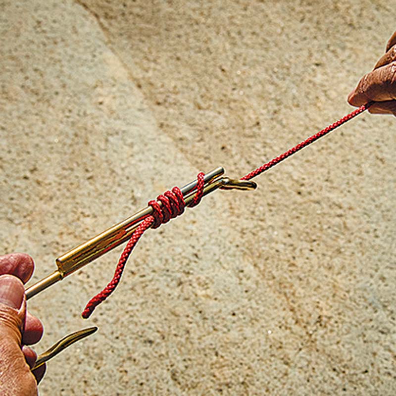 大型の鈎模型を使用し、ハリスに見立てた赤い紐を結び付けている様子