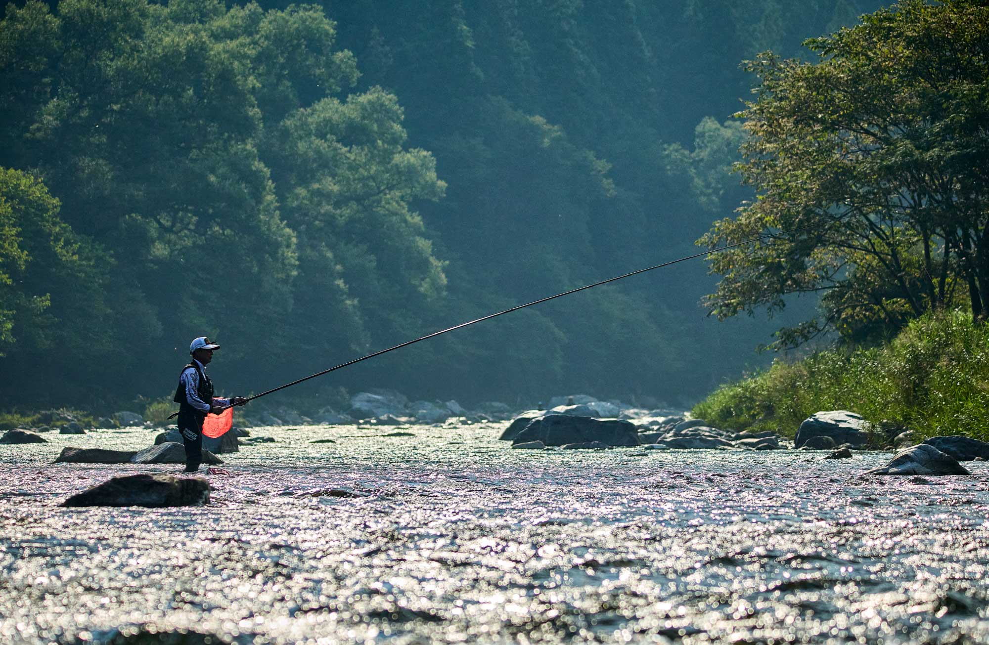 流れのある渓流入り、竿を立てて釣りをする廣岡の空撮