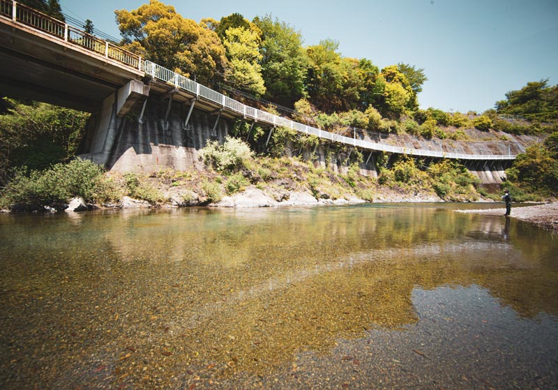 小砂利が多い開けた最下流域と目される広大な下流の景色と、その中で釣りをする廣岡