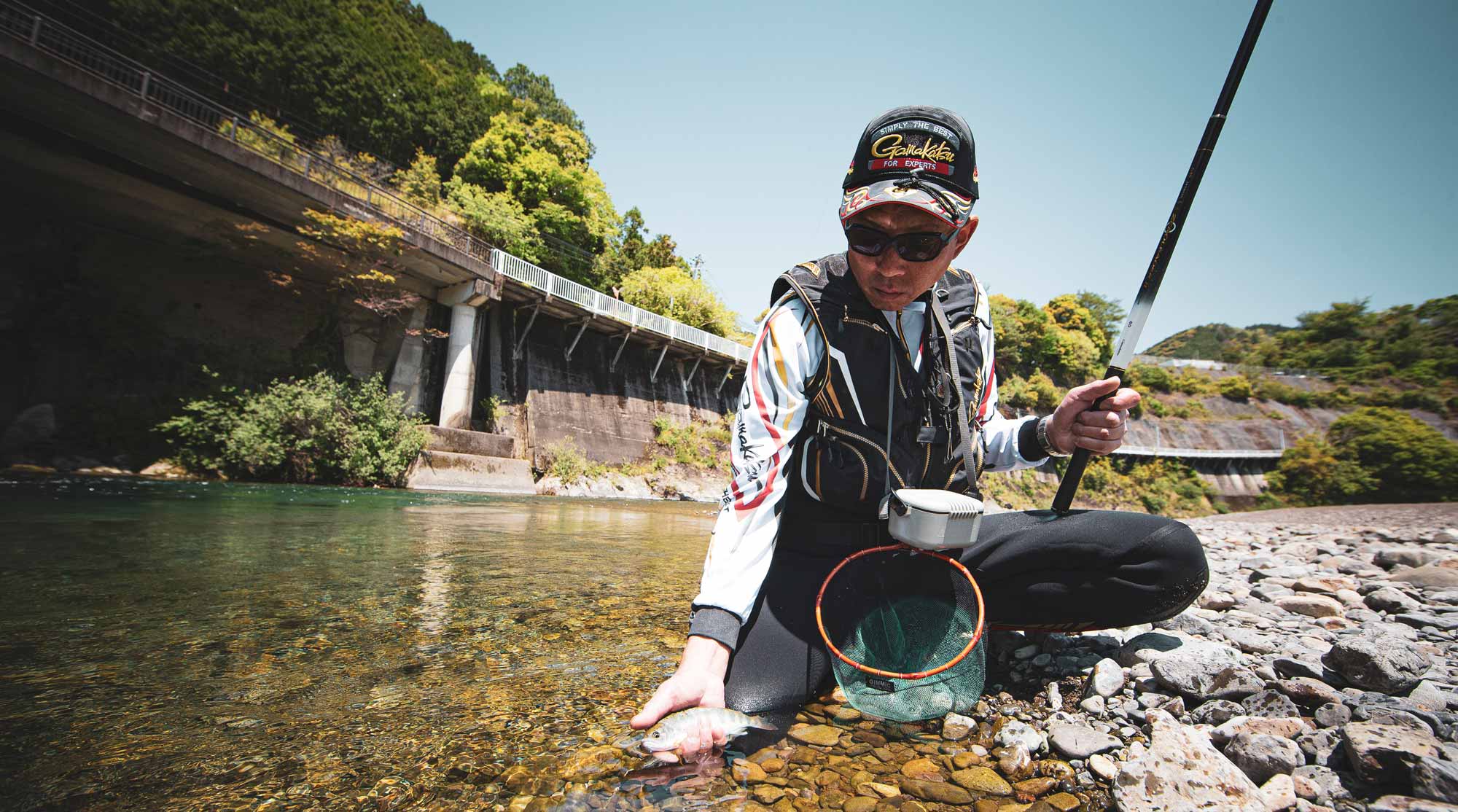 しゃがみ込み、左手内に収まっている魚を見つめる廣岡