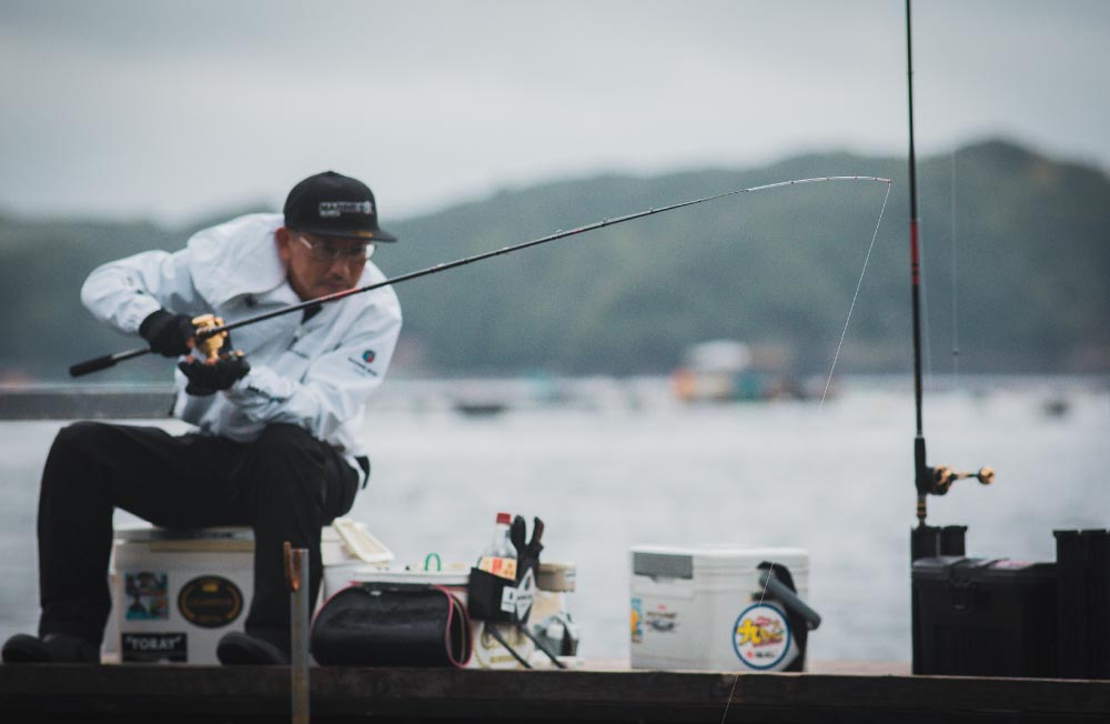 仕掛けの入った海中を注視しながら竿を操作する林
