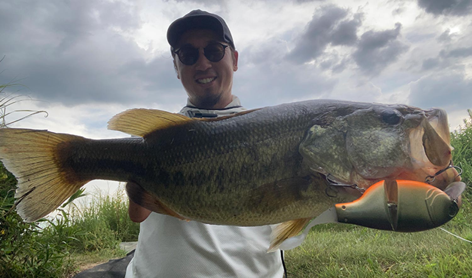 ルアーを唇に引っ掛けた大型のバスを両手で持ち、笑顔の赤松