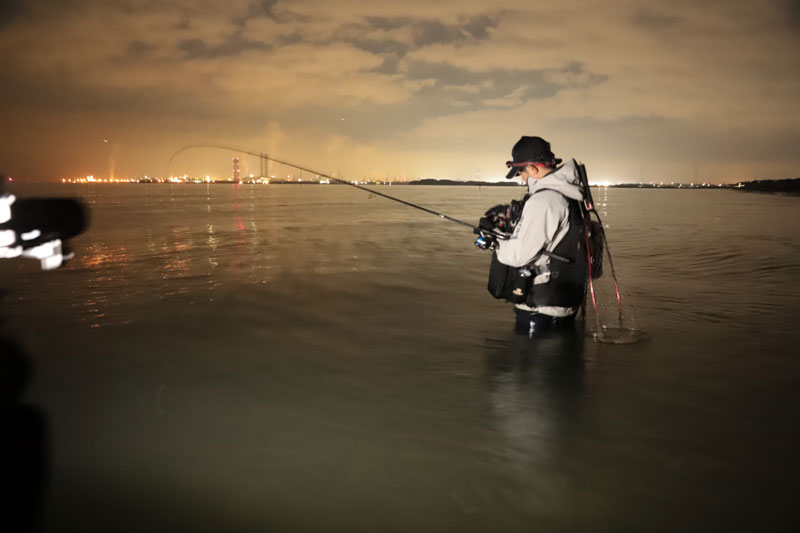 夕暮れ。腰近くまで海に入り、竿を注視しながら釣りをする久保田
