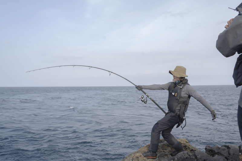 磯上にて、体を大きく反らし魚の引きに耐える松本