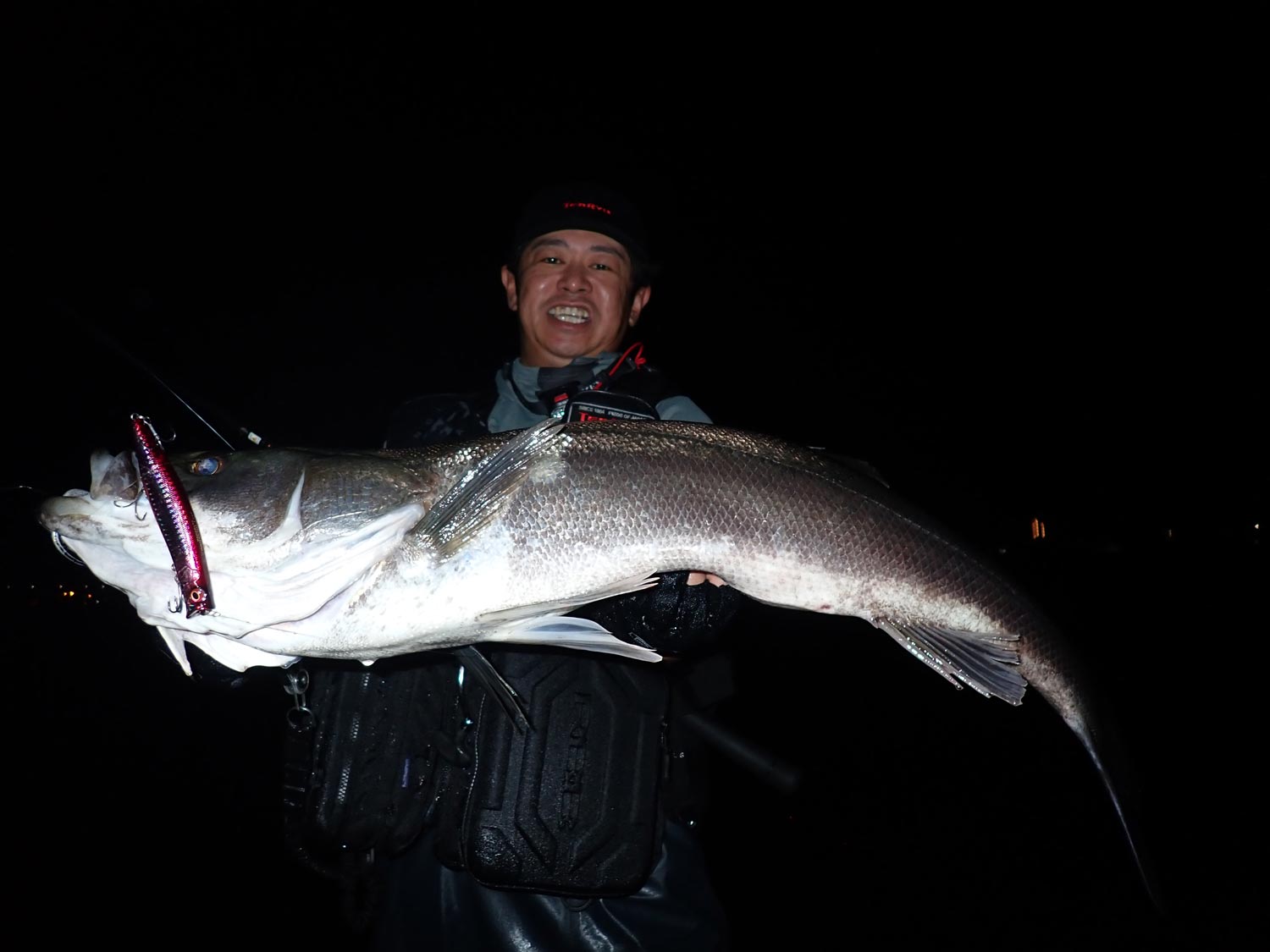 釣り上げたシーバスを両手で掲げ、笑顔を見せる久保田。