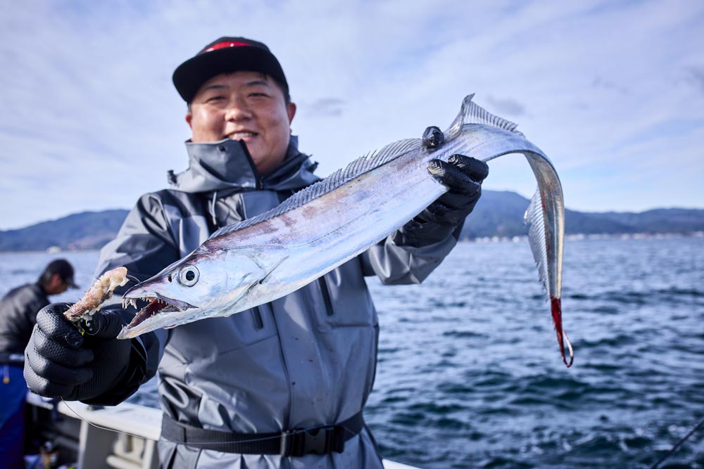 釣り上げた太刀魚を両手で持ち、笑顔の中山