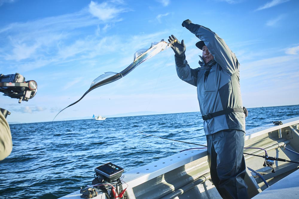 左手に持ったラインを引き、空を泳ぐように舞う釣り上げたタチウオを手元へと寄せる中山