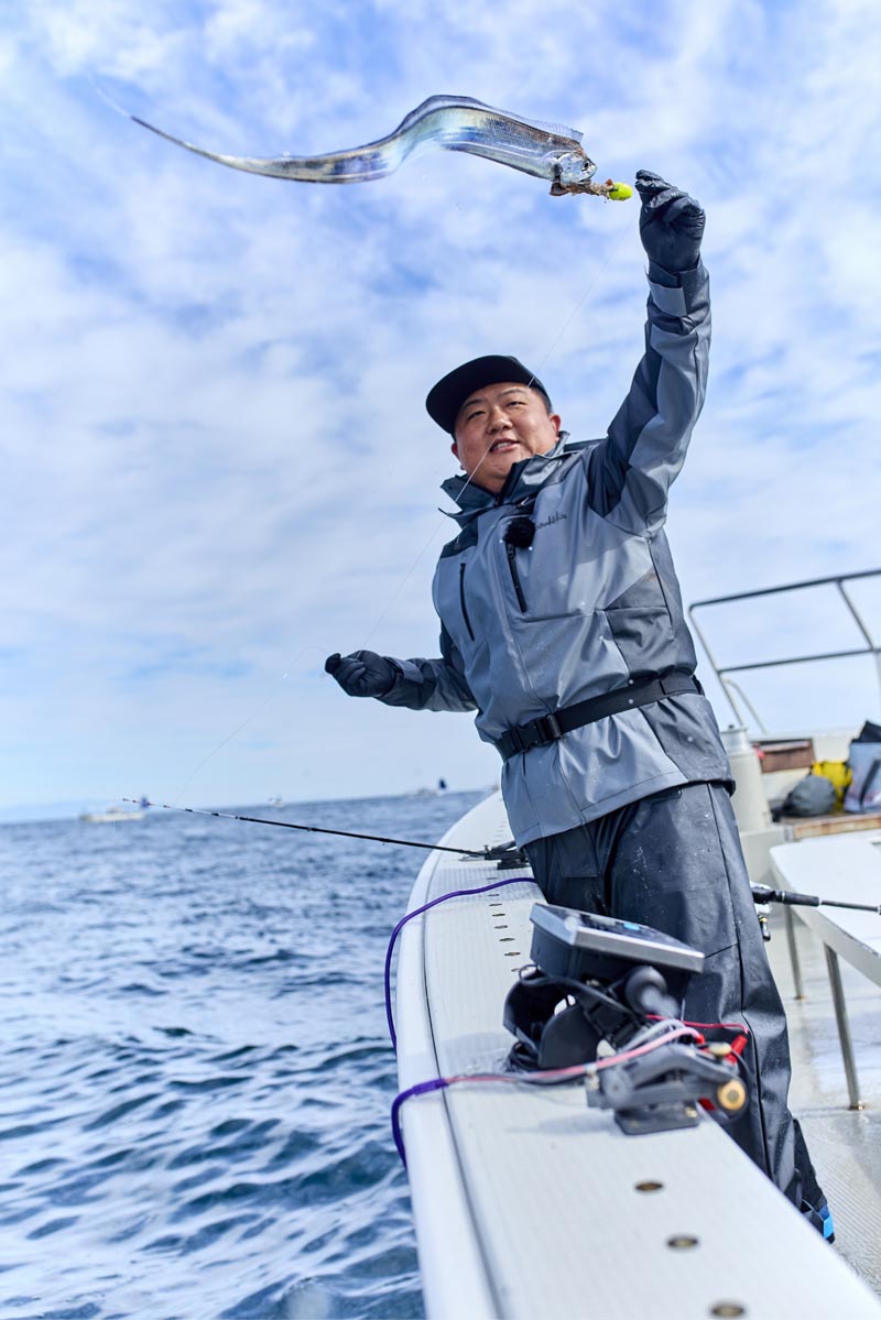 左手に持ったラインを引く中山と、空を泳ぐように舞う釣り上げたタチウオ