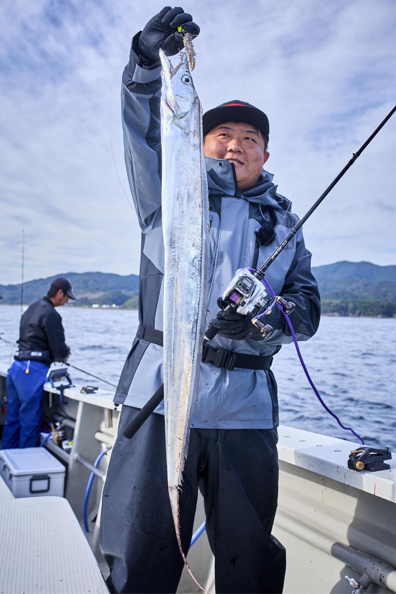 釣り上げたタチウオを右手に、左手に竿を持つ中山"