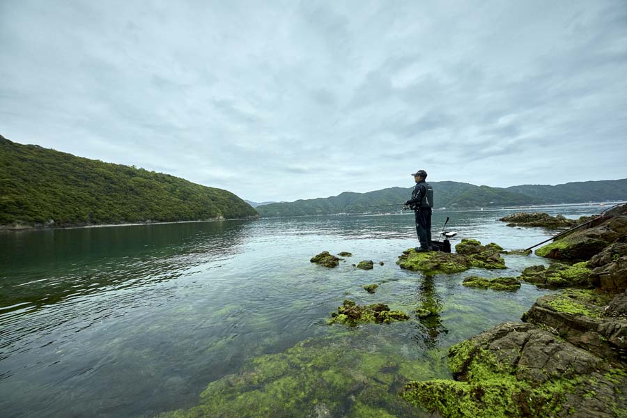 海藻の生えた磯に立ち釣りをする沖永