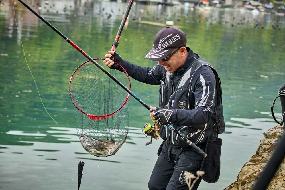 右手に持ったタモ網に収まったチヌを見つめ、笑う沖永