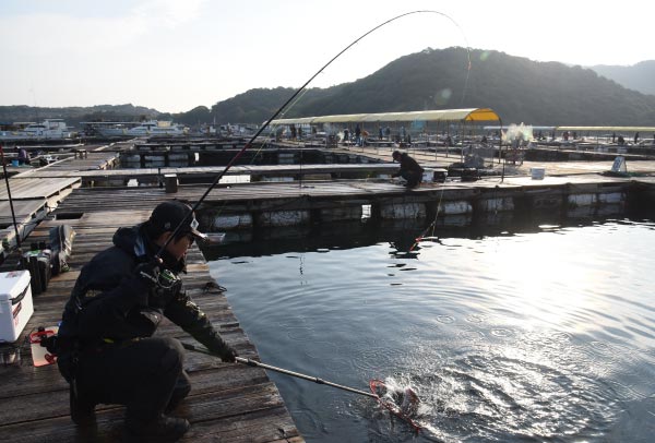 左手に竿を持ち、右手に持ったタモ網に釣り上げた魚を収めようとする中嶋