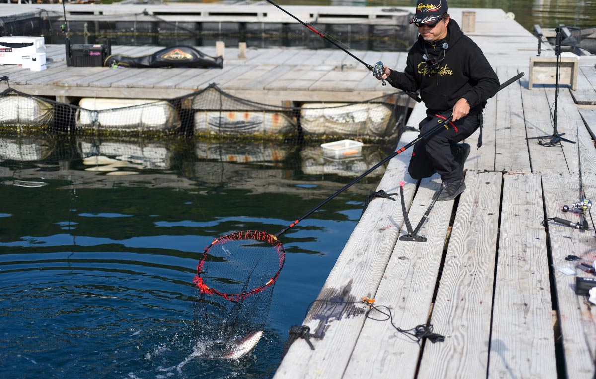 右手に竿を持ったまま、左手のタモで釣り上げた魚を収めた沖長