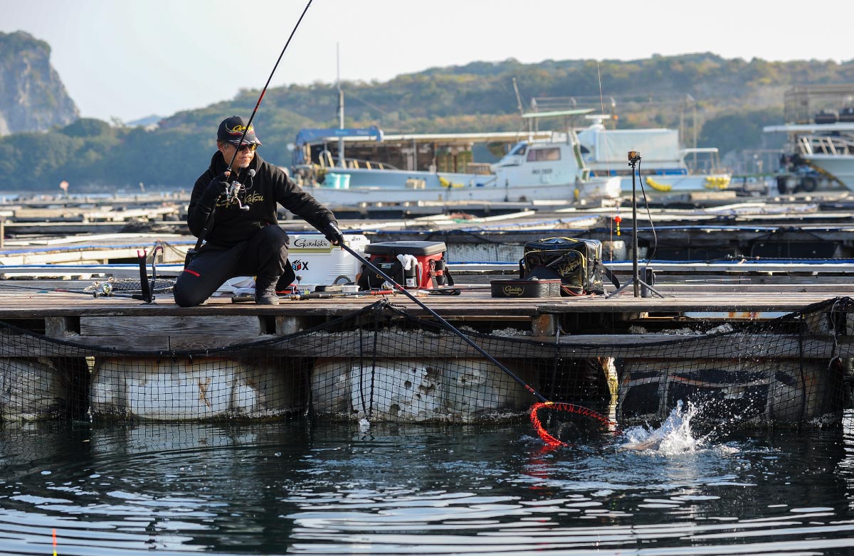 右手に竿を持ったまま、左手のタモで釣り上げた魚を収めようとしている沖長