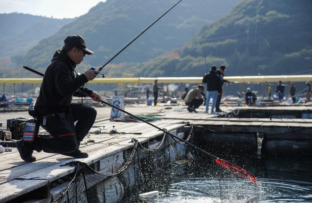 右手に竿を持ったまま、左手のタモに釣り上げたマダイを収めた沖長