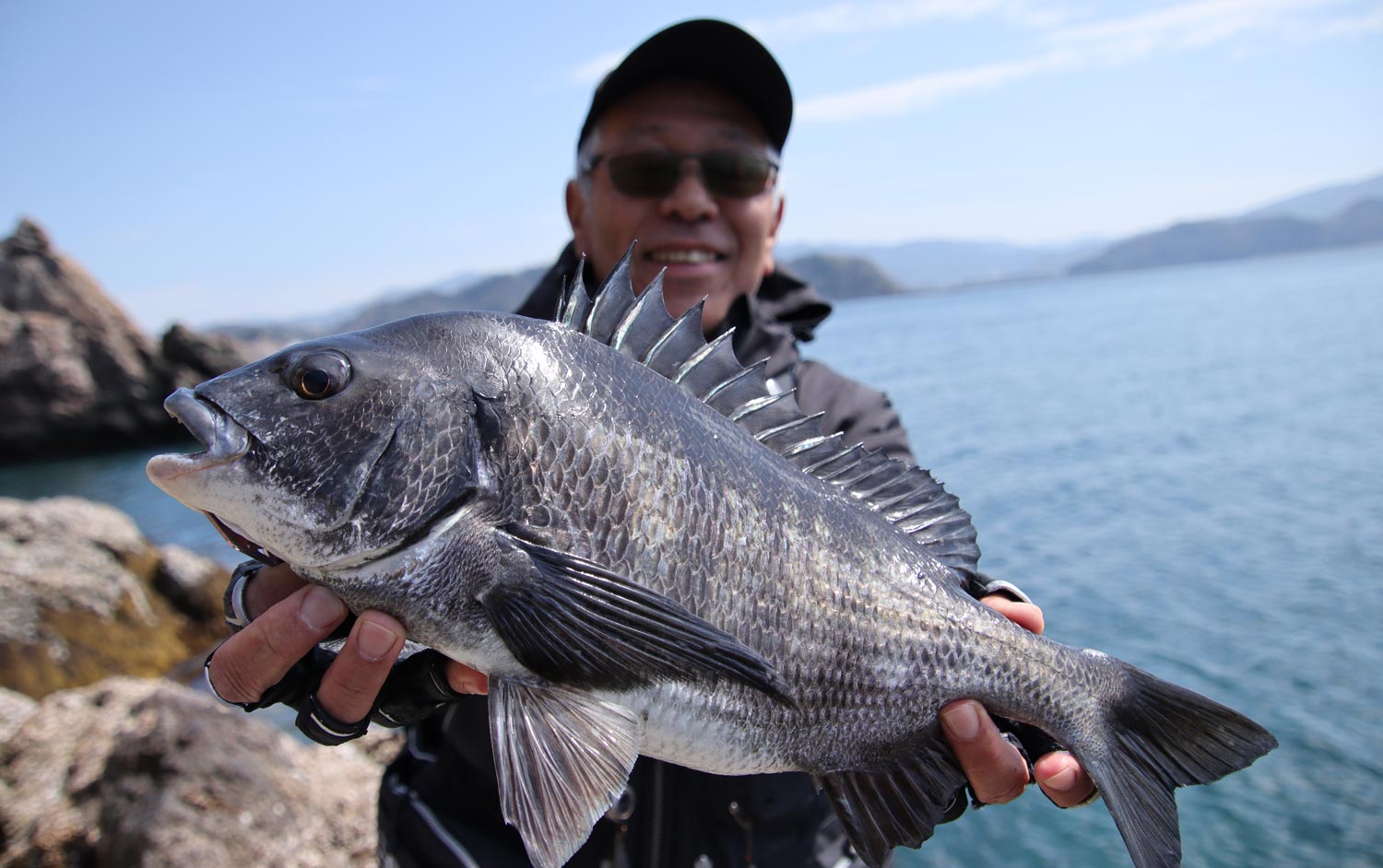 釣り上げたチヌを両手に持ち、笑顔の中西