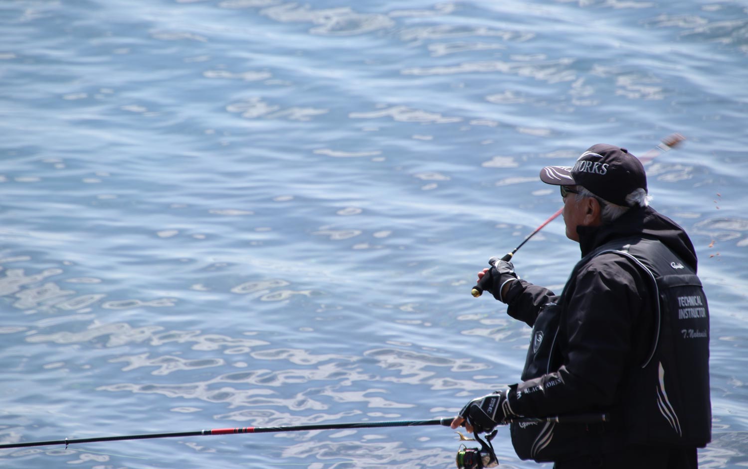 左手に竿を持ち、右手で杓を使いマキ餌をする中西
