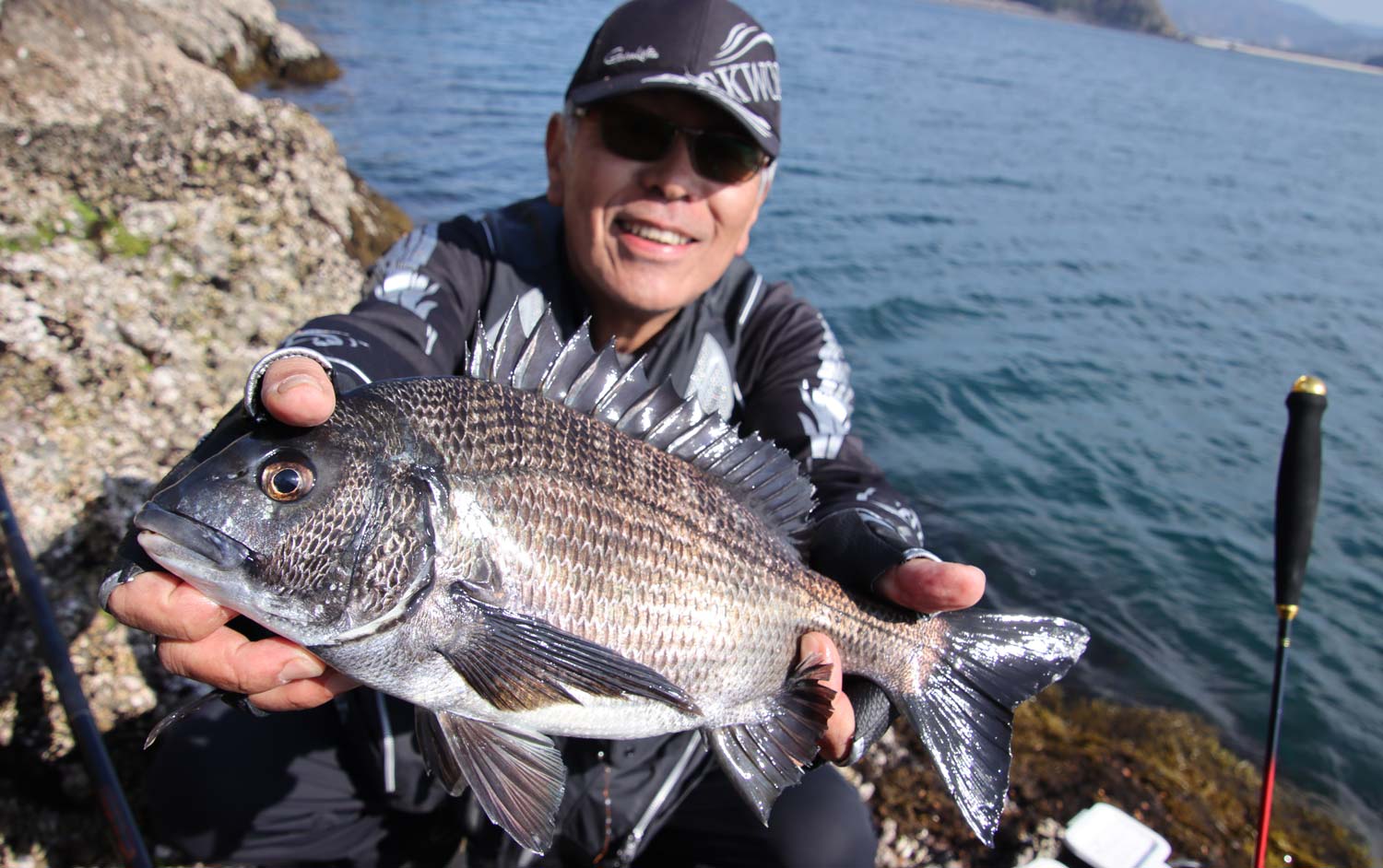 釣り上げたチヌを両手に持ち、笑顔の中西