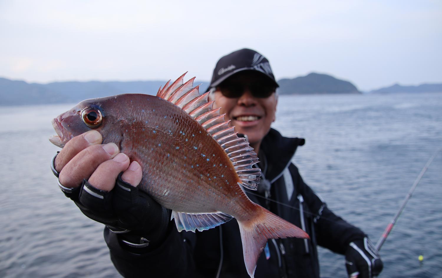 釣り上げたマダイを右手に持ち、笑顔を見せる中西