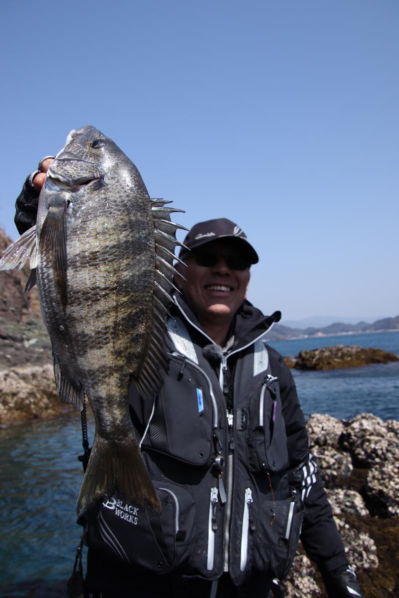 右手で釣り上げたチヌを掲げ、笑顔を見せる中西