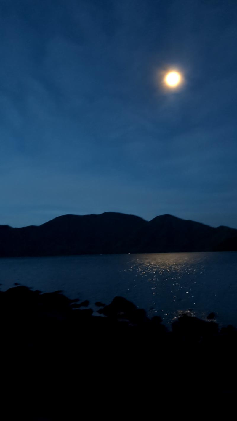 夜明け前でまだ暗い、中禅寺湖の写真。月が煌々と湖面を照らしている。