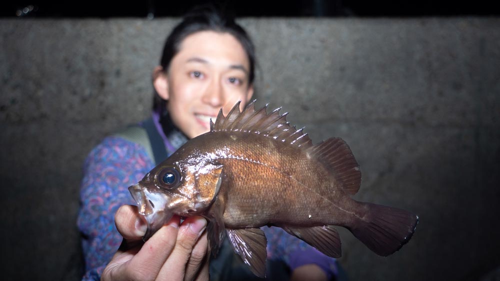 釣り上げた魚を右手で持ち、笑顔の黒神