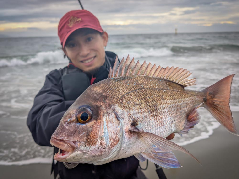 釣り上げたたいを両手で持ち、笑顔の黒神